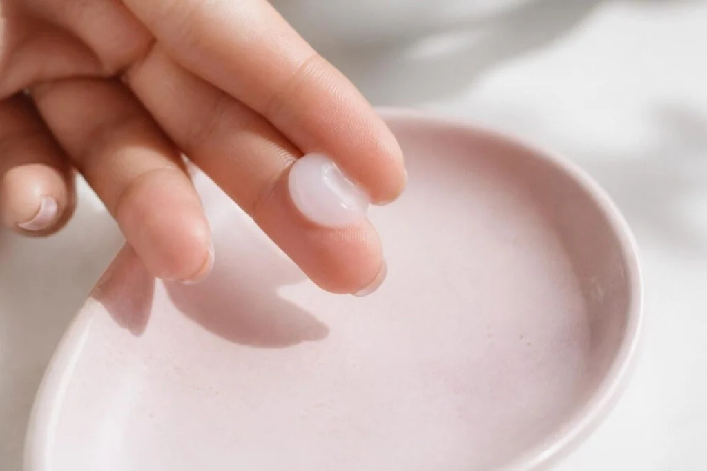 Fingertip holding a dab of light gel non comedogenic sunscreen over a pink ceramic dish