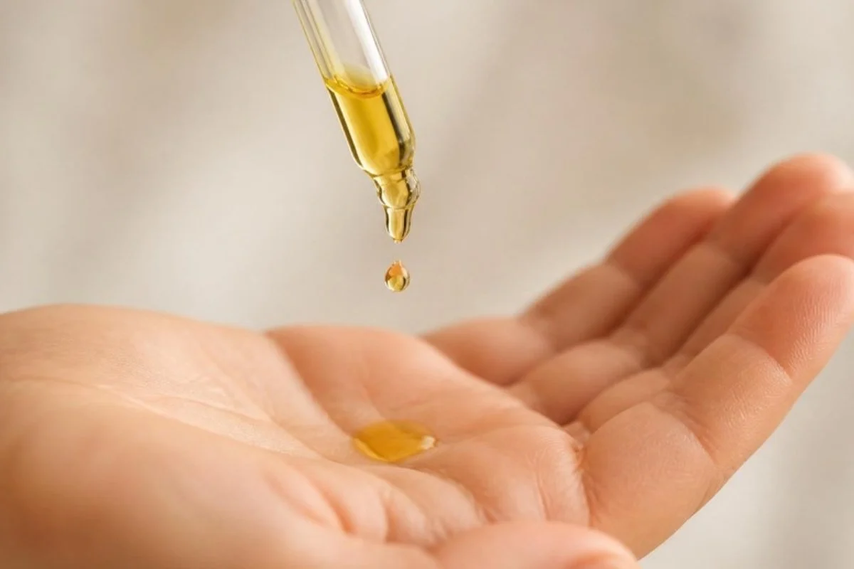 Drop of jojoba oil hair treatment falling from a dropper onto the palm of a hand