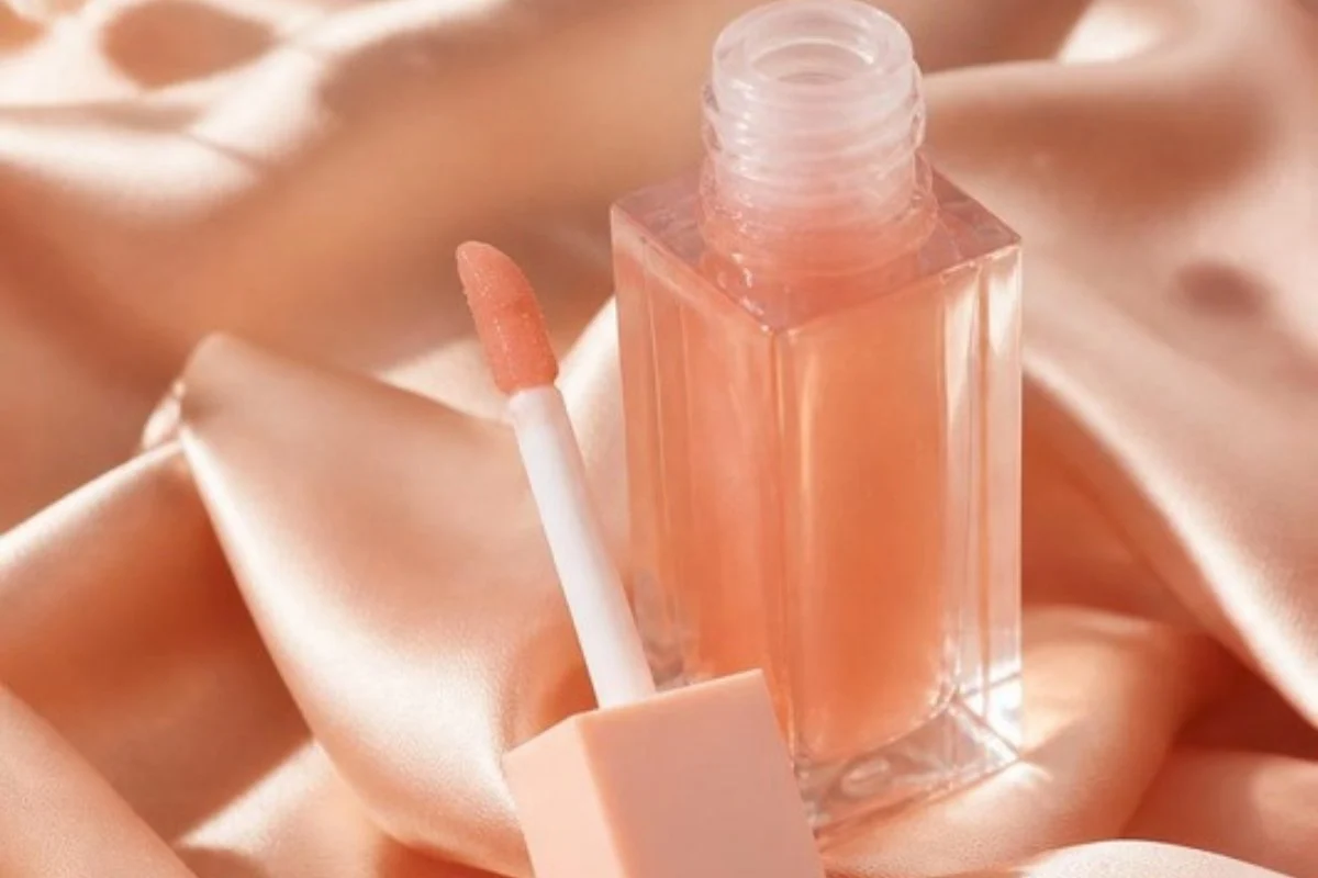 Lip oil bottle with a doe-foot applicator on peach silk