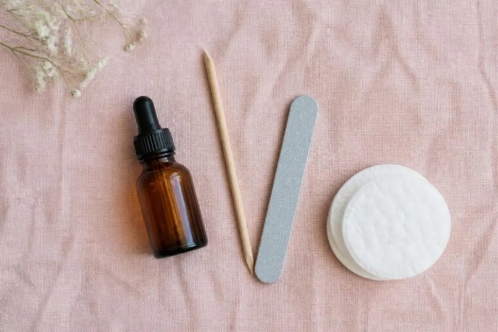 Amber dropper bottle of cuticle oil with a wooden cuticle stick, nail file and cotton pads