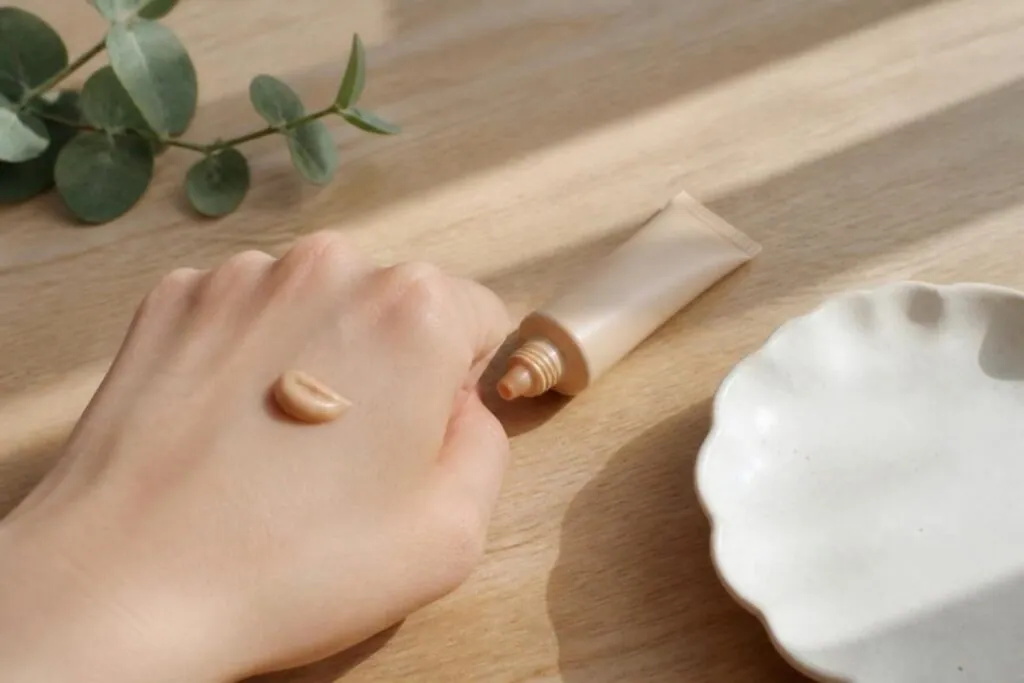 Tube of tinted moisturizer with a swatch on the back of a hand on a wooden table